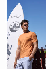 Mann in hellblauem T-Shirt mit Côte d’Azur Surf Team Aufdruck und weißen Shorts.