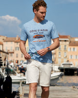 Mann in hellblauem T-Shirt mit Côte d’Azur Surf Team und weißen Shorts.