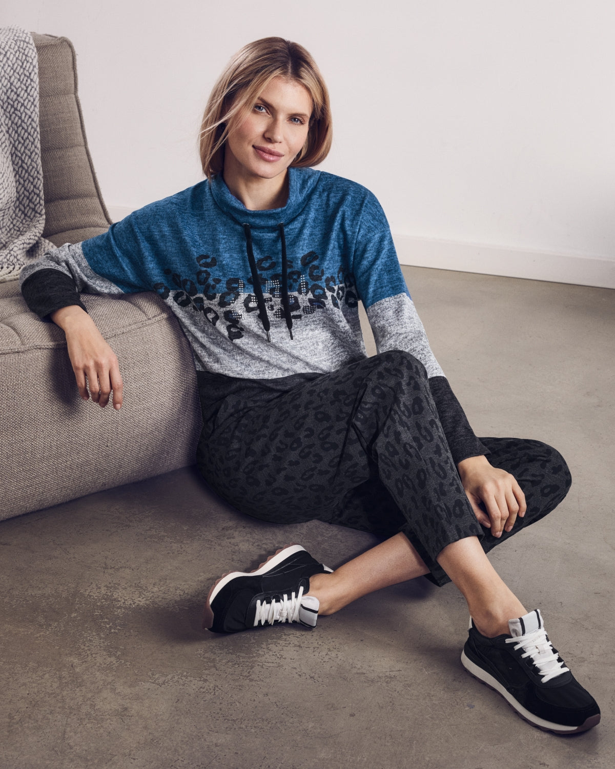 Frau in blauem, grauem und schwarzem Leopardenmuster-Cowl Neck Top und schwarzer Leopardenmuster-Caprihose mit schwarzen und weißen Sportschuhen.