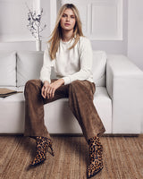 Frau in weißem Sweatshirt, brauner Hose und Stiefeln mit Leopardenmuster.