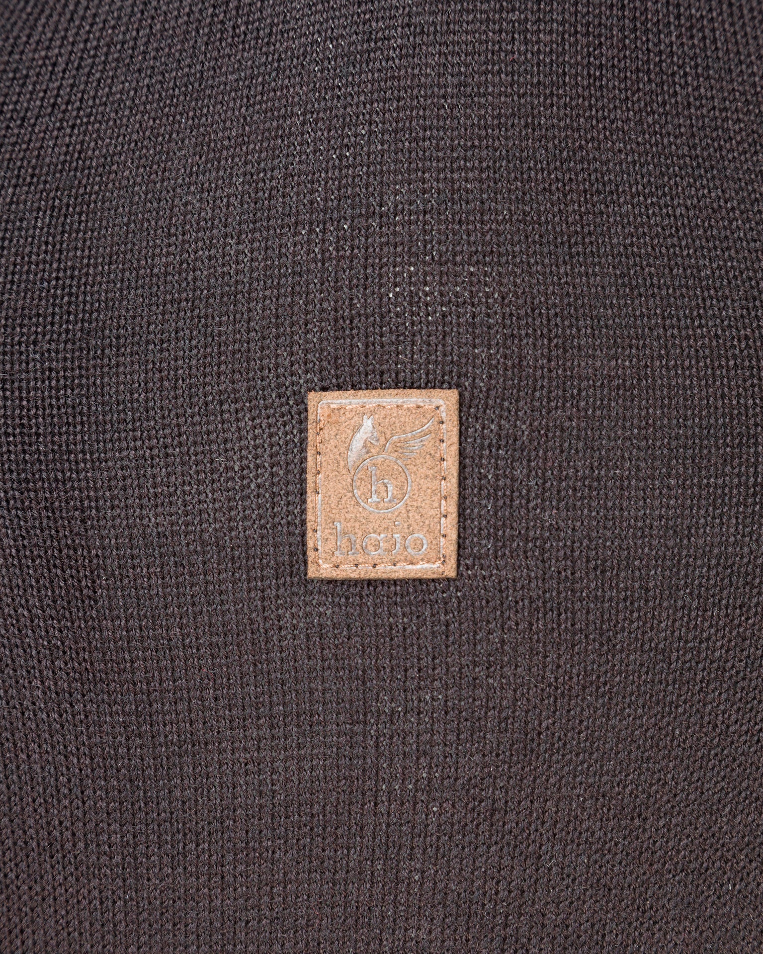 Brauner Lederaufnäher mit Logo auf dunklem Strickstoff.