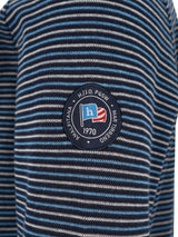 Blau-weiß gestreiftes Poloshirt mit einem runden Logo, das den Buchstaben ’h’ in Rot, Weiß und Blau zeigt.
