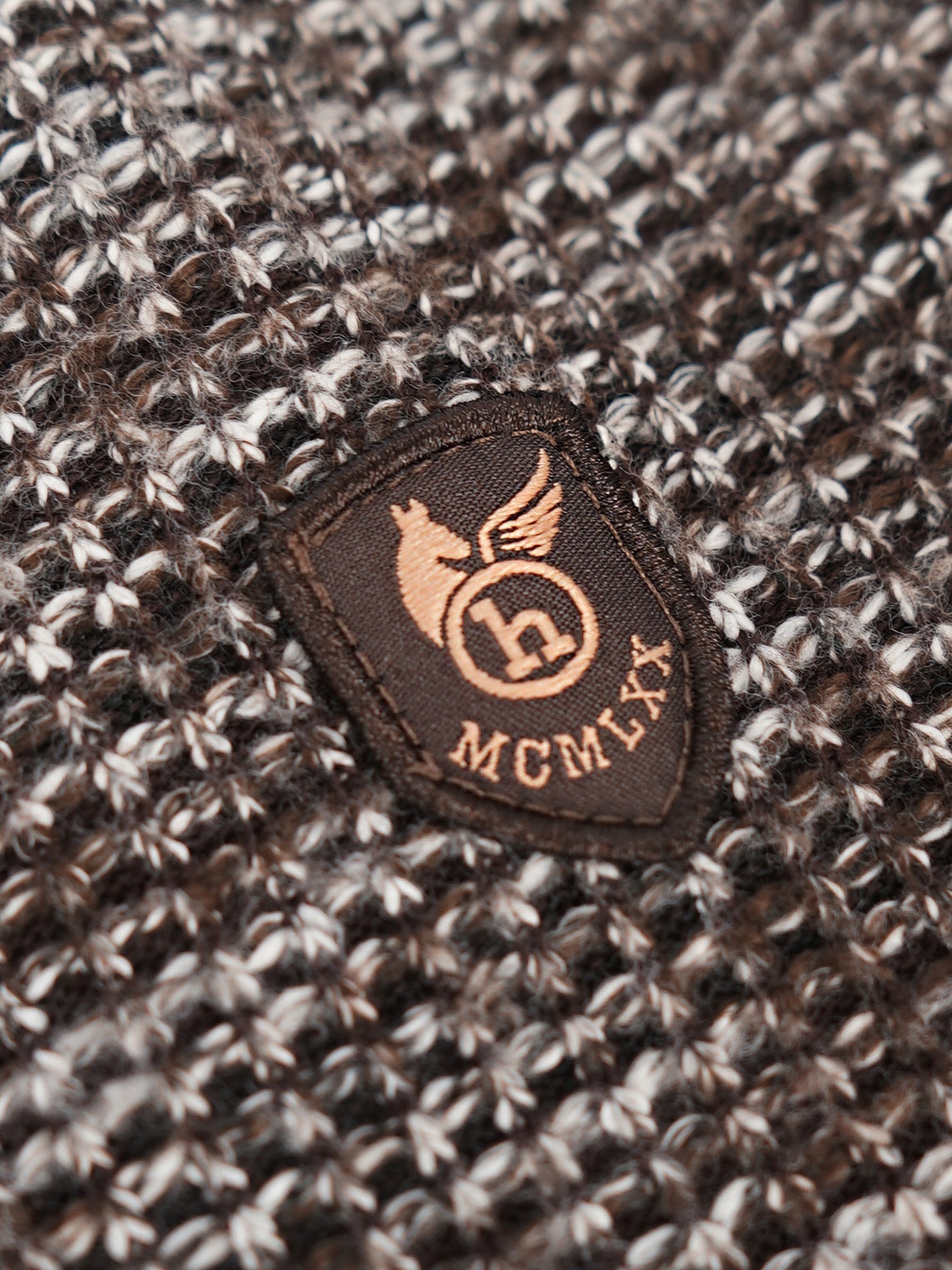 Braune schildförmige patch mit goldfarbenem geflügeltem pferd und mcmxix auf dunkelbraun-weißem strickjacke mit nyloneinsätzen im vorderteil