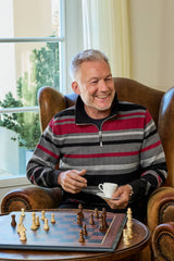 Ein mann sitzt lächelnd mit einem weißen keramikkaffeebecher in einem rot grau schwarz gestreiften troyersweatshirt