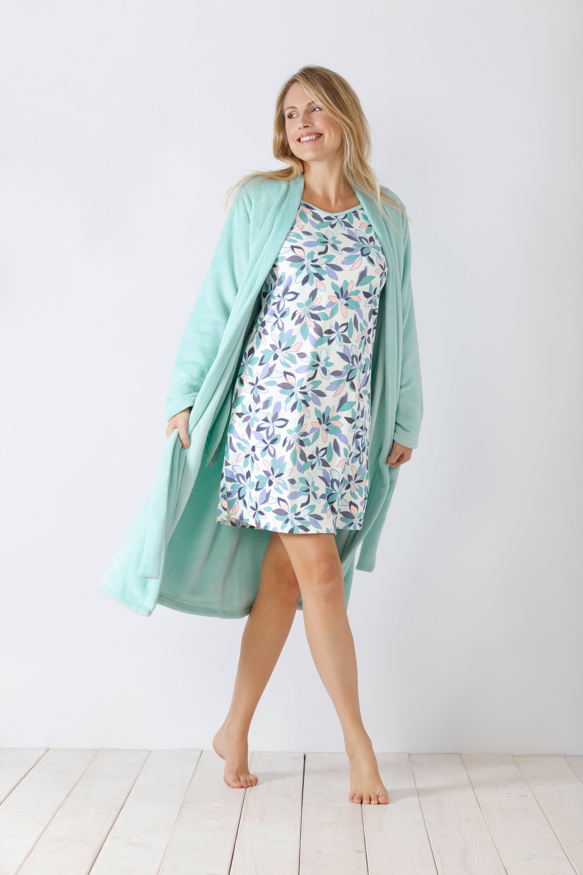 Eine Frau, die ein blaugrünes Gewand über einem weißen Nachthemd mit Blättermuster trägt.