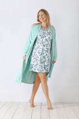 Eine Frau trägt einen rosa Bademantel über einem geblümten Nachthemd.