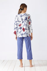 Weißes langärmeliges Oberteil mit Blumendruck und violette Caprihose für Damen als Pyjama-Set.
