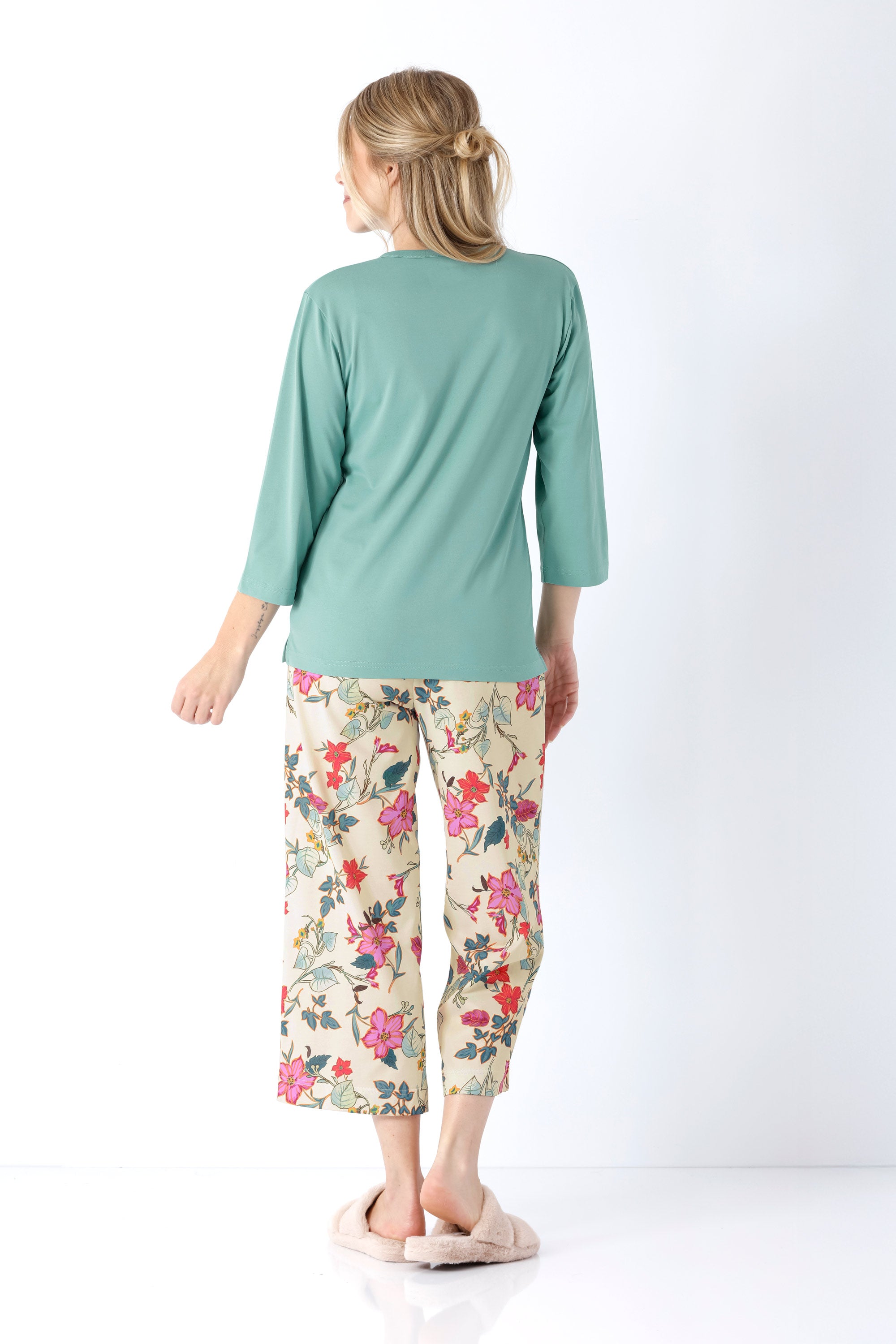 Eine frau trägt einen damen schlafanzug mit teal farbenem langarmshirt und caprihosen mit buntem blumenmuster