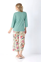 Eine frau trägt einen damen schlafanzug mit teal farbenem langarmshirt und caprihosen mit buntem blumenmuster