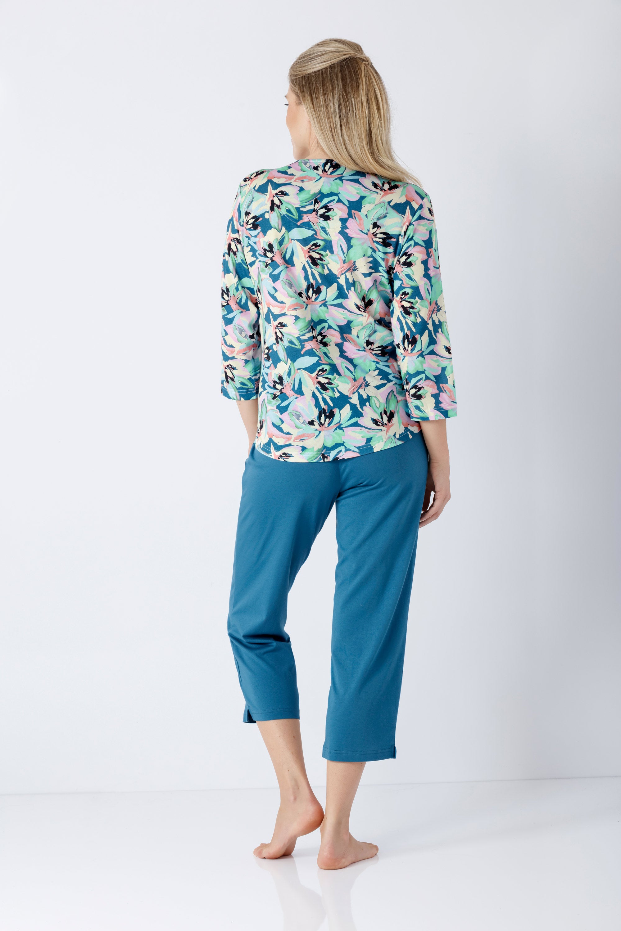 Eine frau trägt einen damen schlafanzug 7 8 aus premium baumwolle tencel modal mit floralem oberteil und türkis caprihose