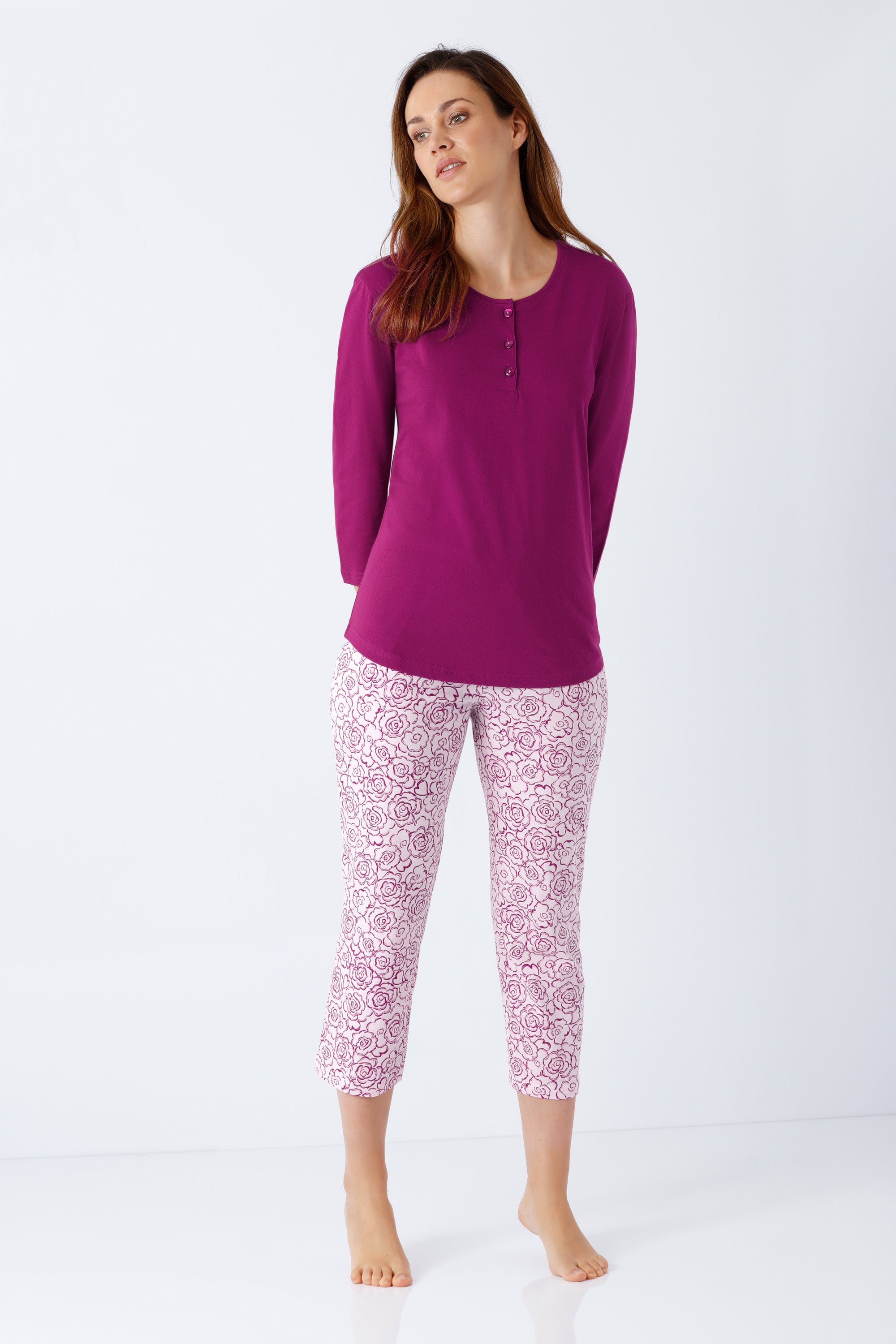 Eine frau trägt einen magentafarbenen langärmligen henley-damen schlafanzug 7/8 aus premium-baumwolle mit rosenmuster caprihose