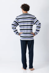 Ein mann trägt den nos herren schlafanzug klima-light® mit gestreiftem langarmoberteil in marine und dunkler hose
