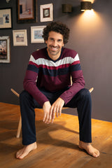 Ein lächelnder Mann mit lockigem dunklem Haar, der ein langärmeliges, gestreiftes Hemd und eine dunkle Hose trägt.