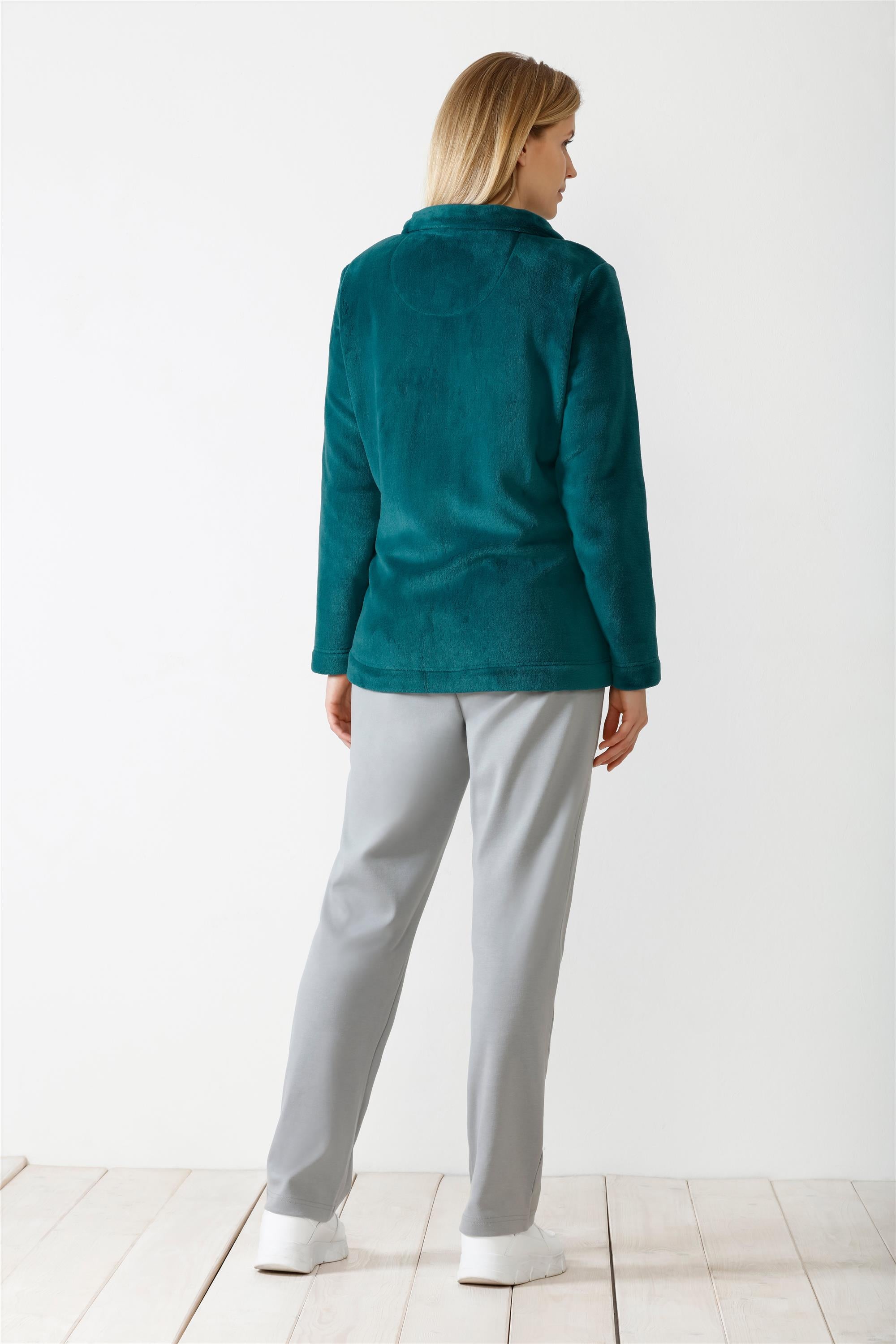 Eine Frau, die ein blaugrünes langärmeliges Fleece-Oberteil und eine graue Hose trägt.