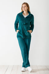 Eine Frau trägt einen blaugrünen Samt-Trainingsanzug mit einer Jacke mit Reißverschluss und einer passenden Hose.