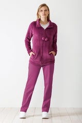 Eine Frau in einem magentafarbenen, plüschigen Trainingsanzug mit Reißverschluss und einem weißen T-Shirt darunter.