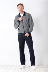 Graue Herren-Trainingsjacke mit marineblauem Kragen und Manschetten, gepaart mit einer marineblauen Trainingshose und weißen Turnschuhen.