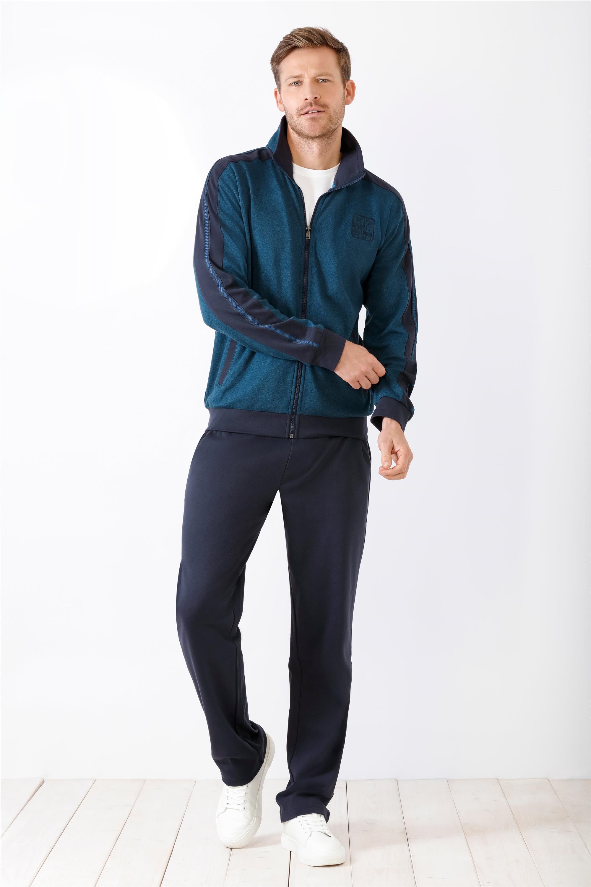 Herren-Trainingsanzug in Petrol und Marineblau mit durchgehendem Reißverschluss, weißem Unterhemd und weißen Sneakers.