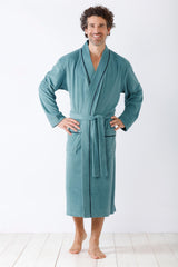 Ein lächelnder Mann in einem langen, blaugrünen Bademantel mit schwarzem Saum und gebundener Taille.