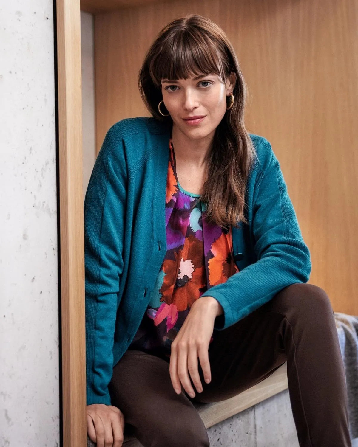 Tealfarbene Strickjacke mit geblümter Bluse und brauner Hose.