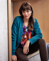 Tealfarbene Strickjacke mit geblümter Bluse und brauner Hose.