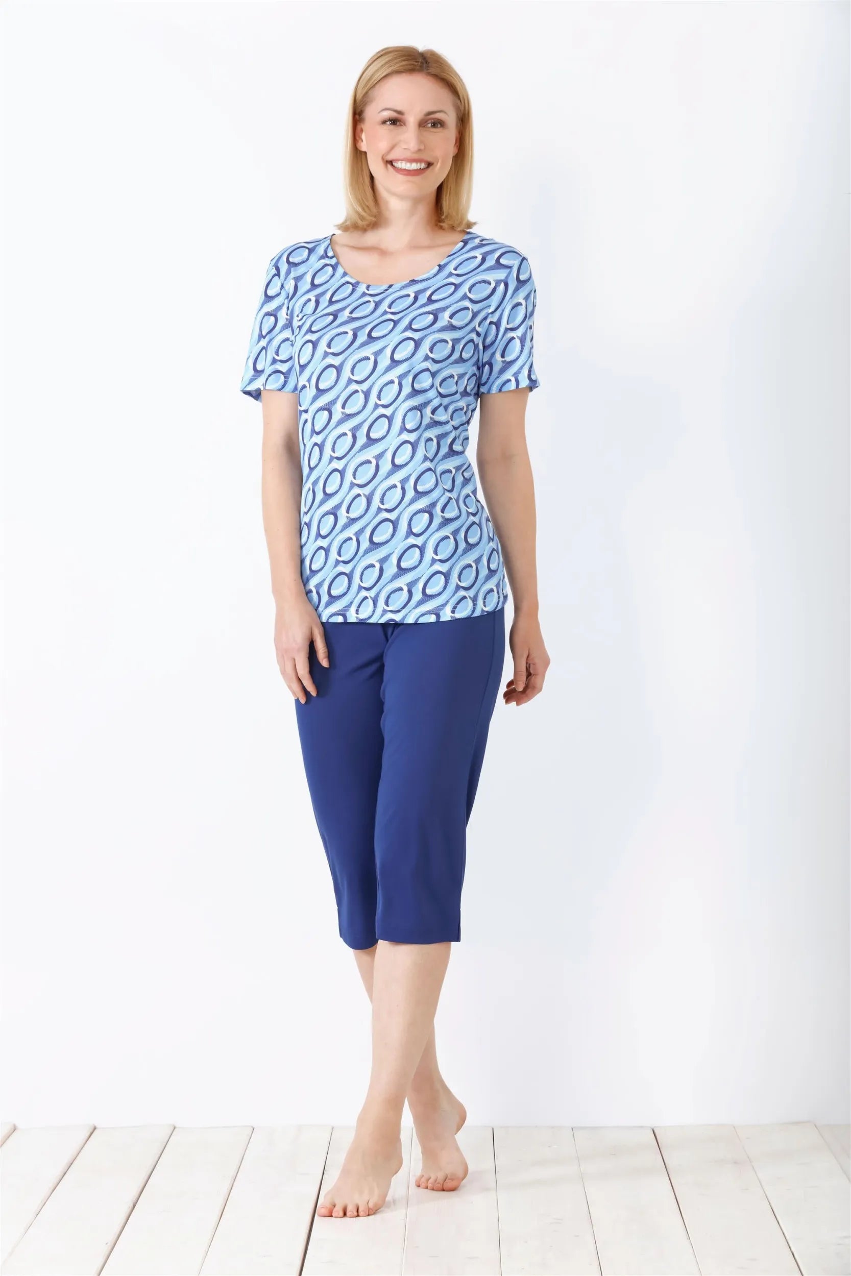 Blau gemustertes kurzärmeliges Oberteil einer Frau und einfarbige blaue Caprihose.