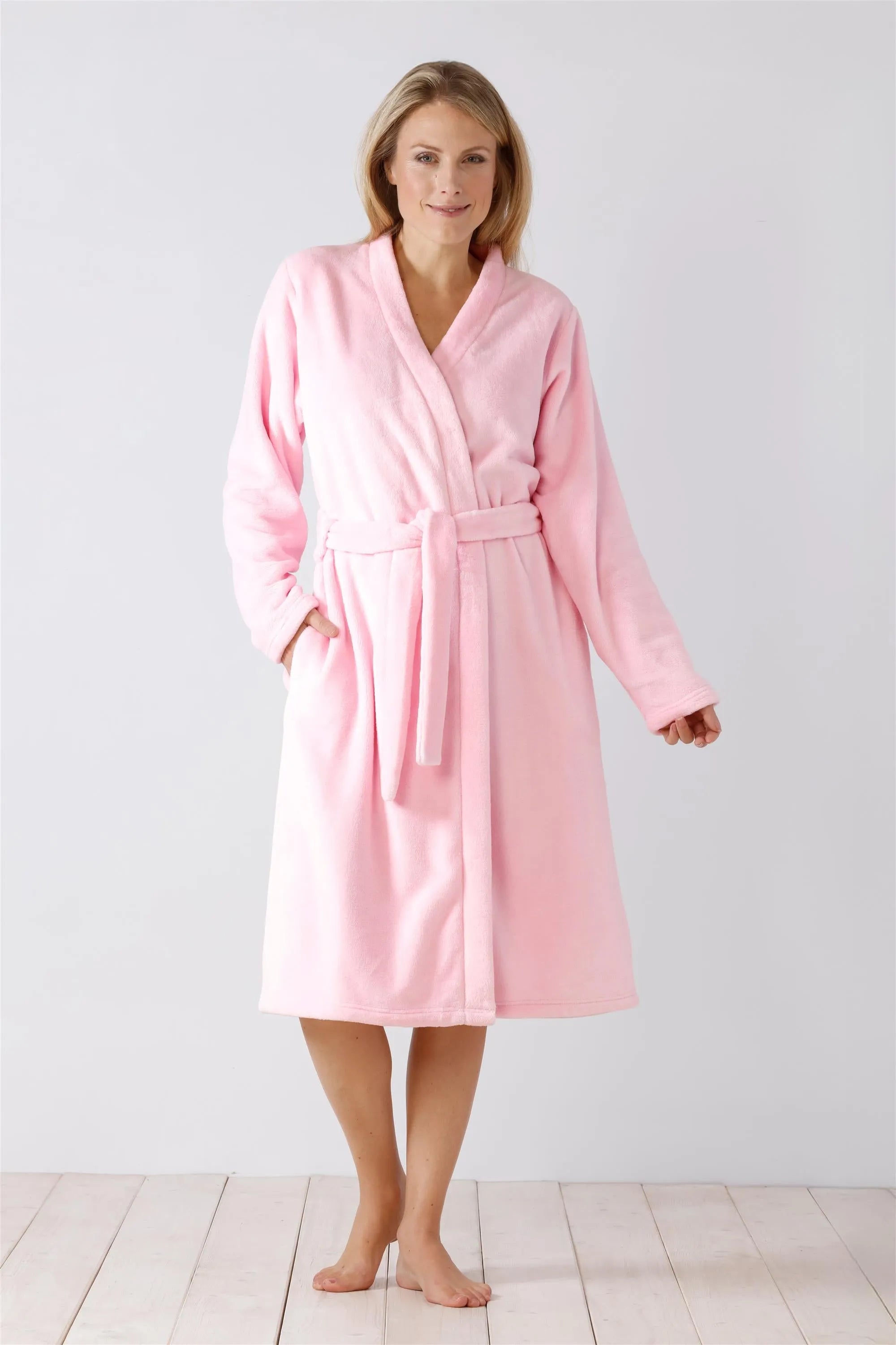 Eine Frau modelliert einen weichen rosa Fleece-Bademantel mit Schnürung und Taschen.