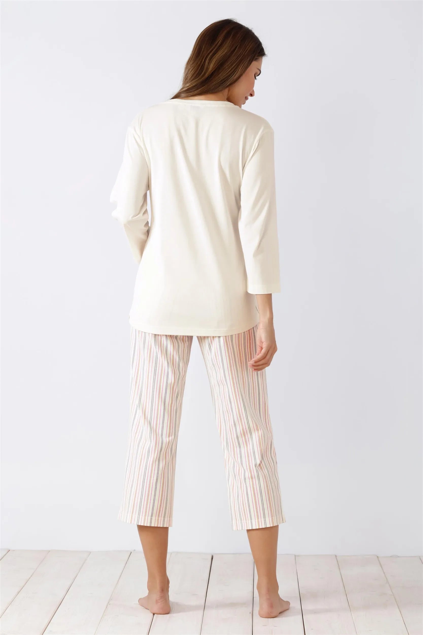 Langärmeliges cremefarbenes Oberteil und gestreifte Caprihose für Damen als Schlafanzug.