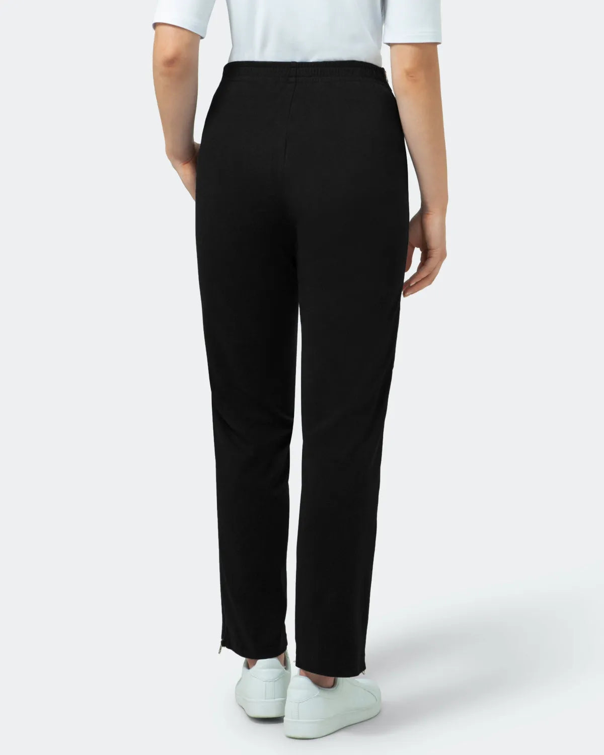 Schwarze Hose mit geradem Bein und hoher Taille und weißem Saum, dazu weiße Sneakers.
