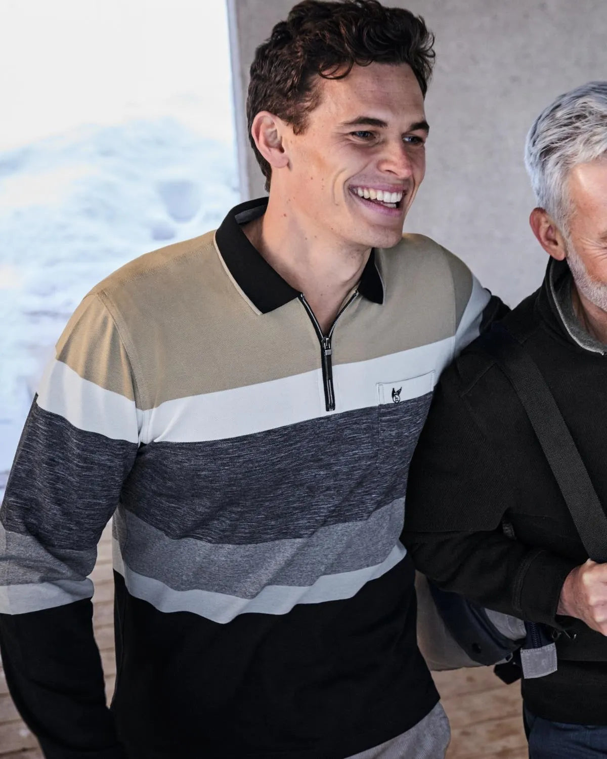 Gestreiftes Poloshirt mit Viertelreißverschluss, olivgrüne und graue Streifen auf schwarzem Grund.