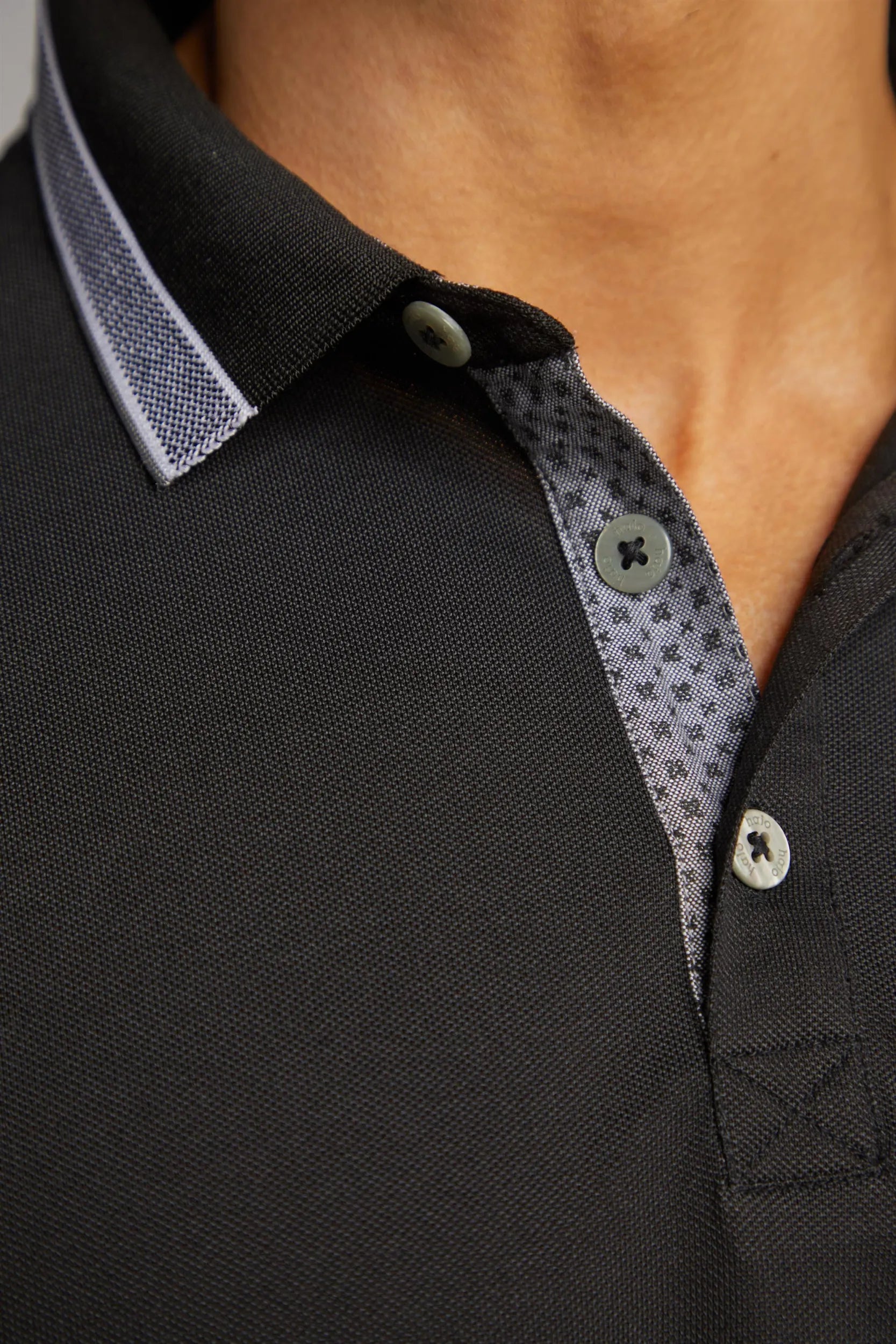 Schwarzes Poloshirt mit weißen Knöpfen und gemustertem Kragen
