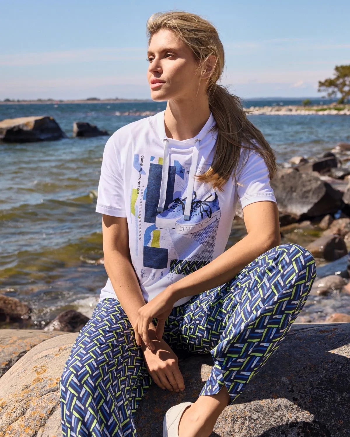 Weißes grafisches T-Shirt mit abstraktem geometrischem Muster und blau gemusterte Hose.