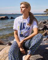 Weißes grafisches T-Shirt mit abstraktem geometrischem Muster und blau gemusterte Hose.