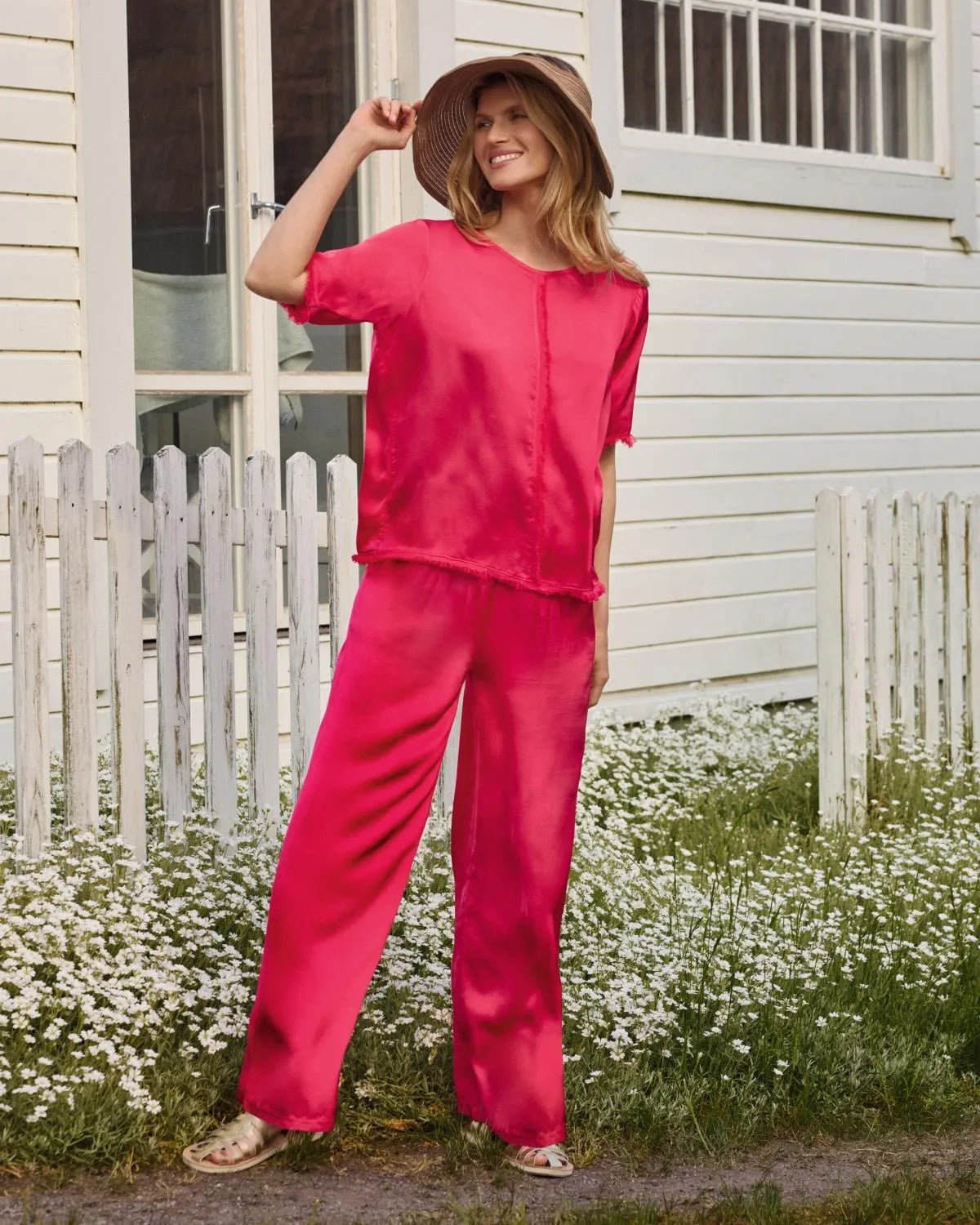 Rosa Seidenpyjama mit passendem breitkrempigen Hut und Sandalen.