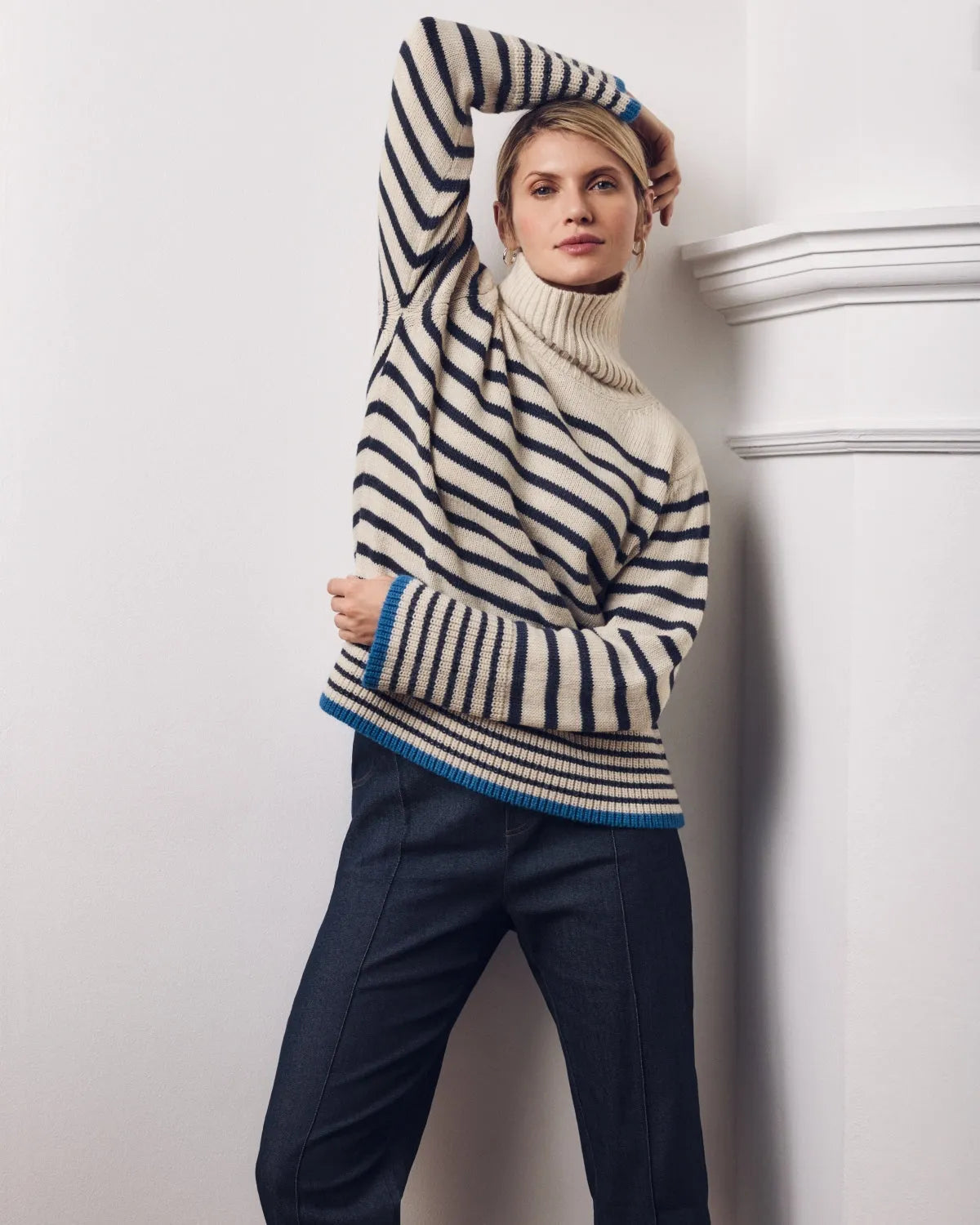 Frau in einem cremefarbenen und marineblauen gestreiften Rollkragenpullover mit blauen Bündchen und Saum sowie einer dunkelblauen Hose.