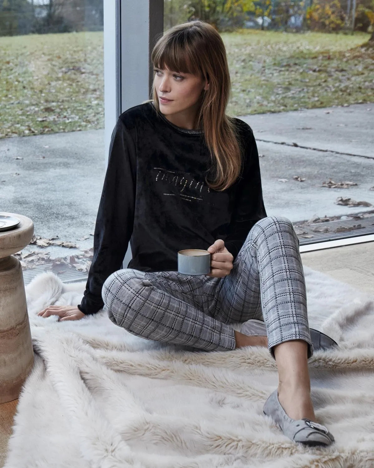 Schwarzes Sweatshirt mit dem Schriftzug ’Das Original’, grau karierte Hose und weißer Flauschteppich.