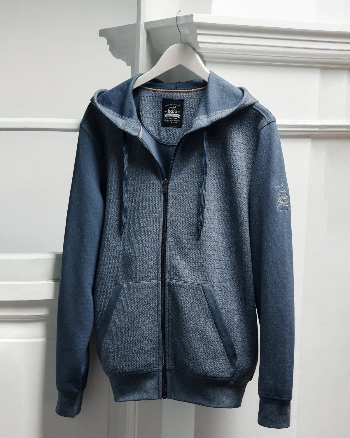 Blauer Kapuzenpullover mit durchgehendem Reißverschluss, strukturiertem Körper und glatten Ärmeln.