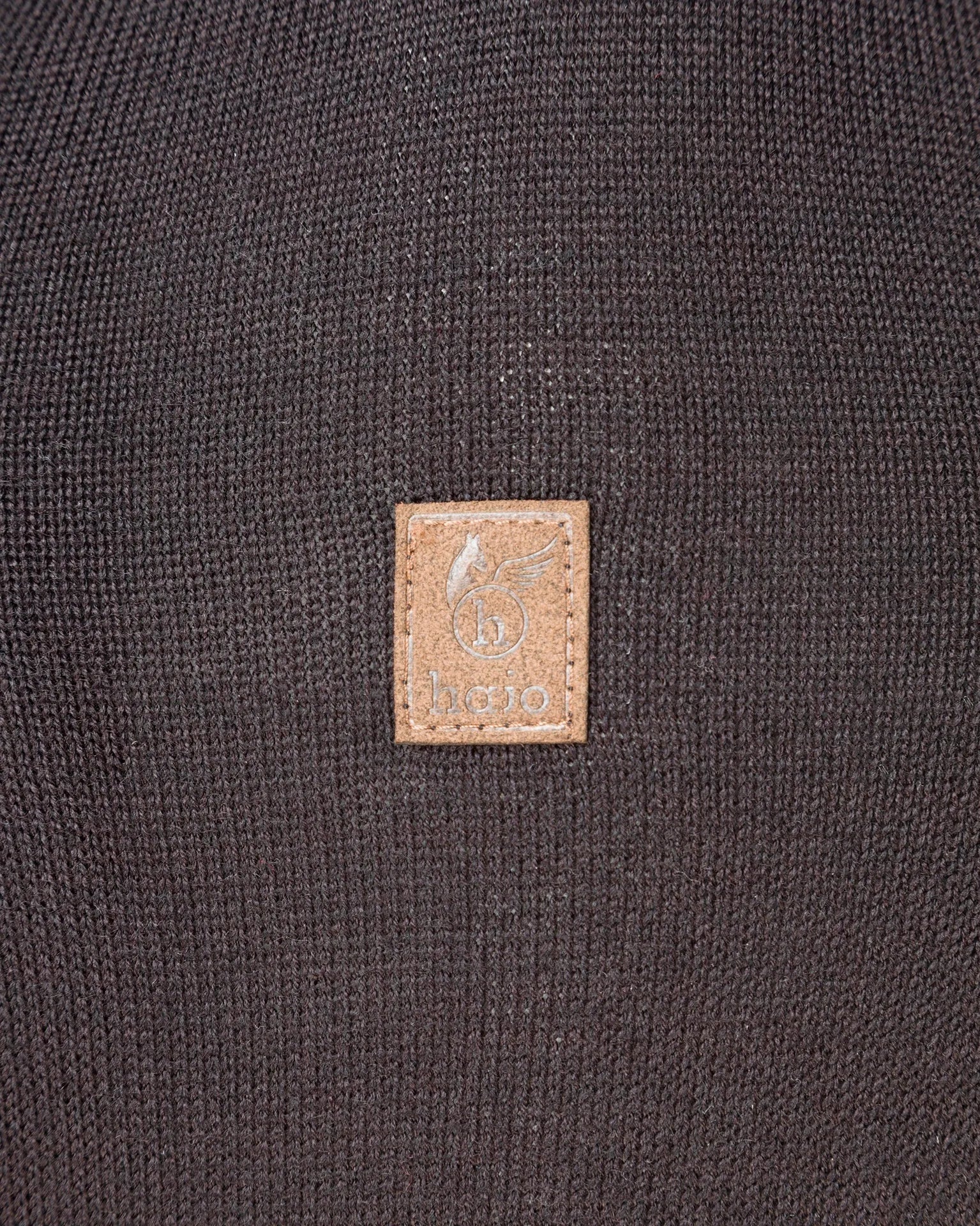 Brauner Lederaufnäher mit Logo auf dunklem Strickstoff.