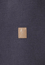 Kleiner brauner Lederaufnäher auf dunklem Stoff.
