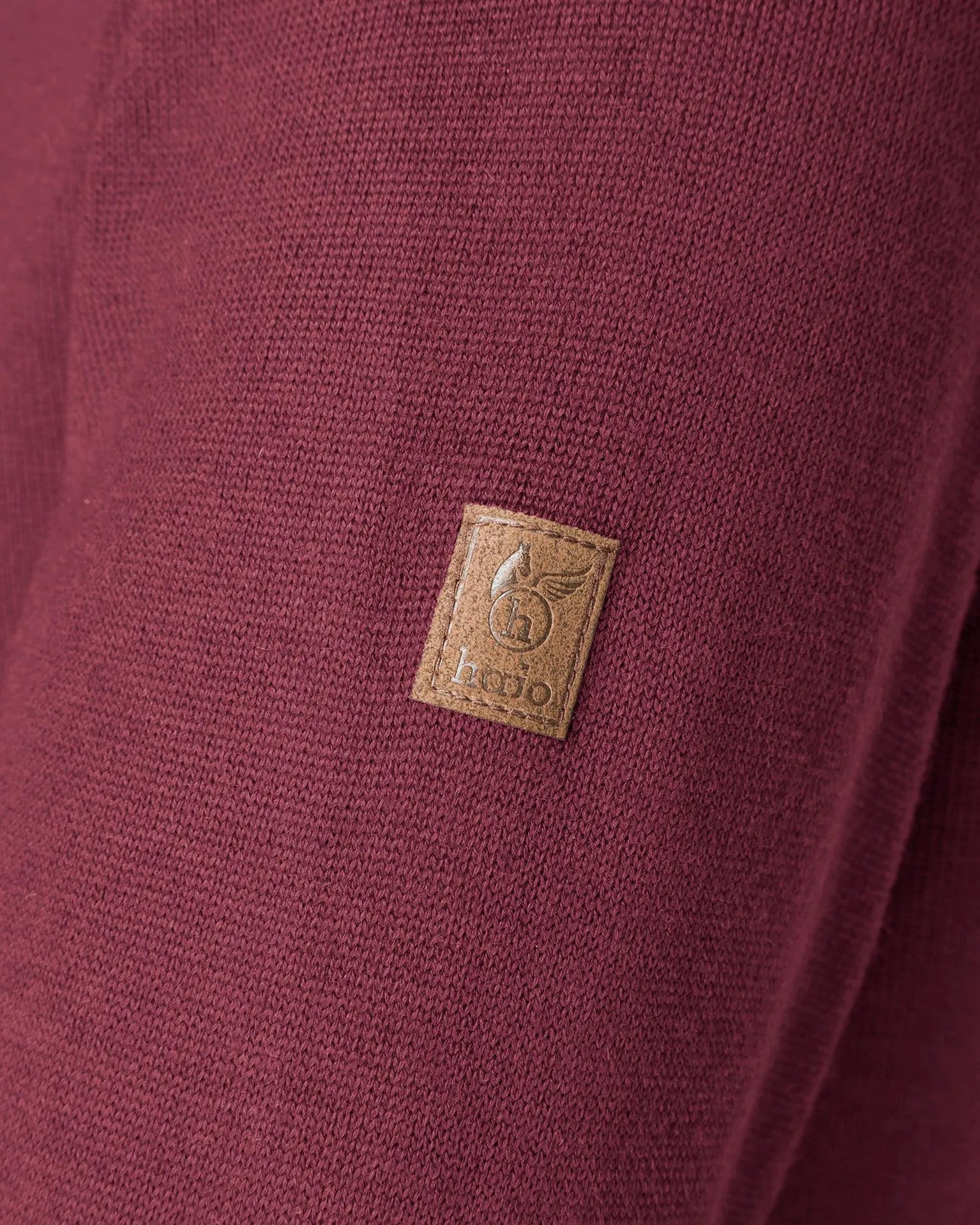 Brauner Lederaufnäher mit aufgenähtem Logo auf weinrotem Stoff.