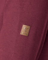 Brauner Lederaufnäher mit aufgenähtem Logo auf weinrotem Stoff.