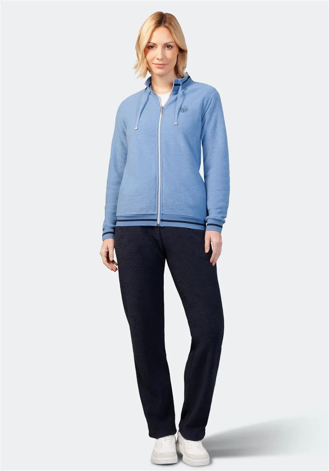 Blauer Kapuzenpulli mit Reißverschluss, schwarze Hose und weiße Turnschuhe.