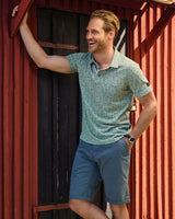 Grün gesprenkeltes Poloshirt mit marineblauen Shorts und rotem Türhintergrund.