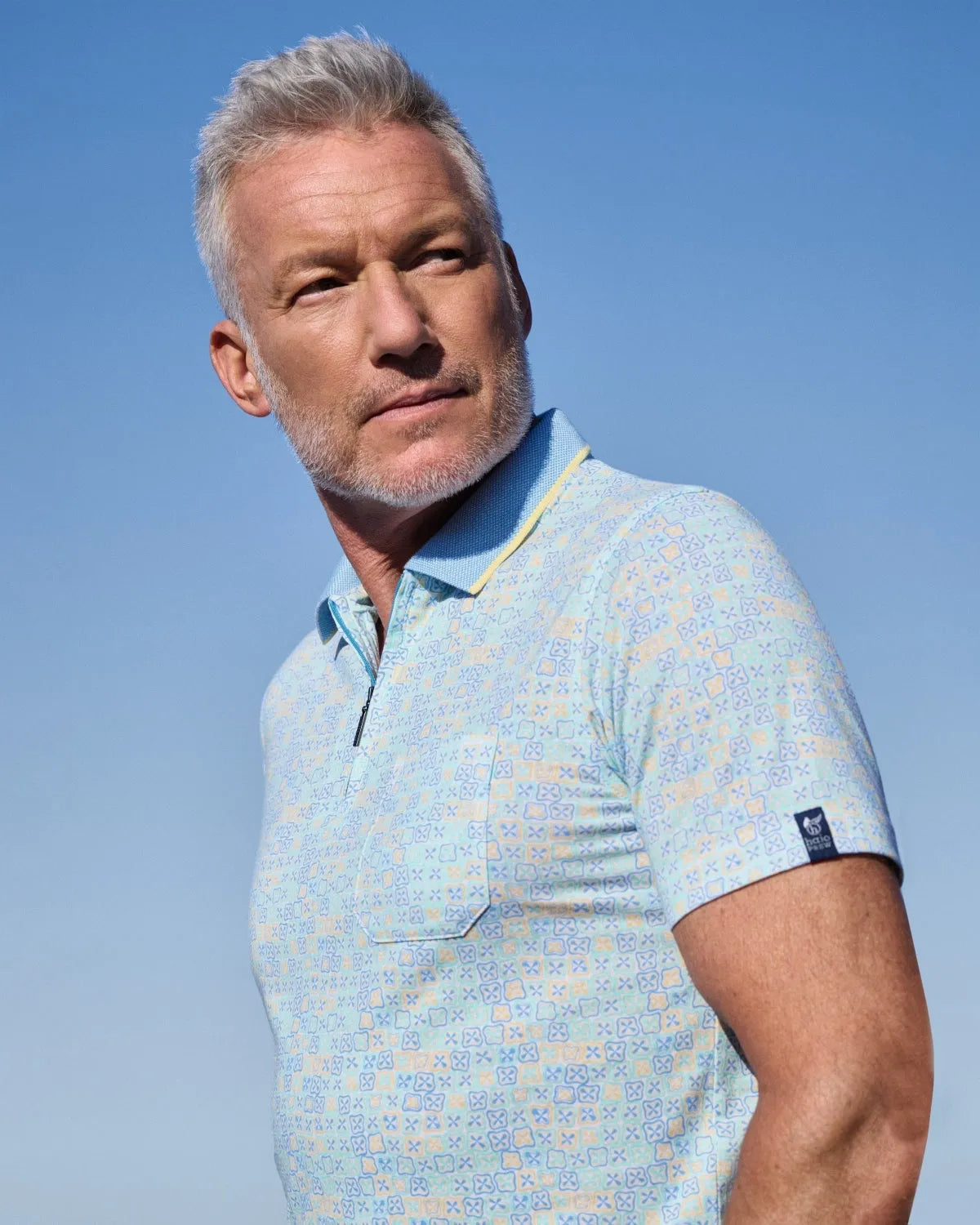 Hellblau gemustertes Poloshirt mit Tasche und Kragen, wahrscheinlich aus Baumwolle oder Polyestergemisch.