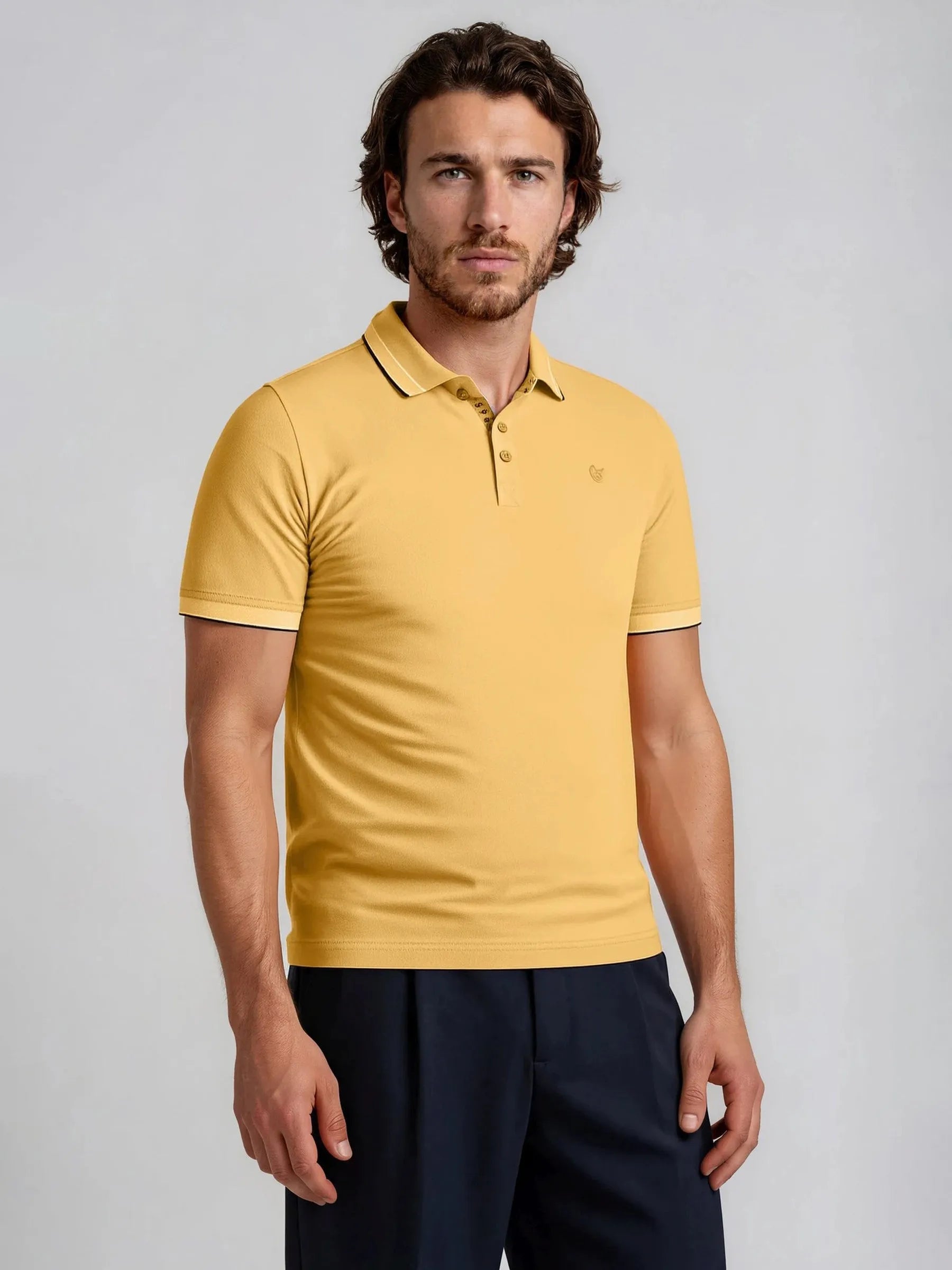 Ein mustard-gelber kurzarm poloshirt capacity pique mit kontrastierendem dunklem kragen und ärmelabschluss sowie kleinem sticklogo auf der brust