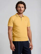 Ein mustard-gelber kurzarm poloshirt capacity pique mit kontrastierendem dunklem kragen und ärmelabschluss sowie kleinem sticklogo auf der brust