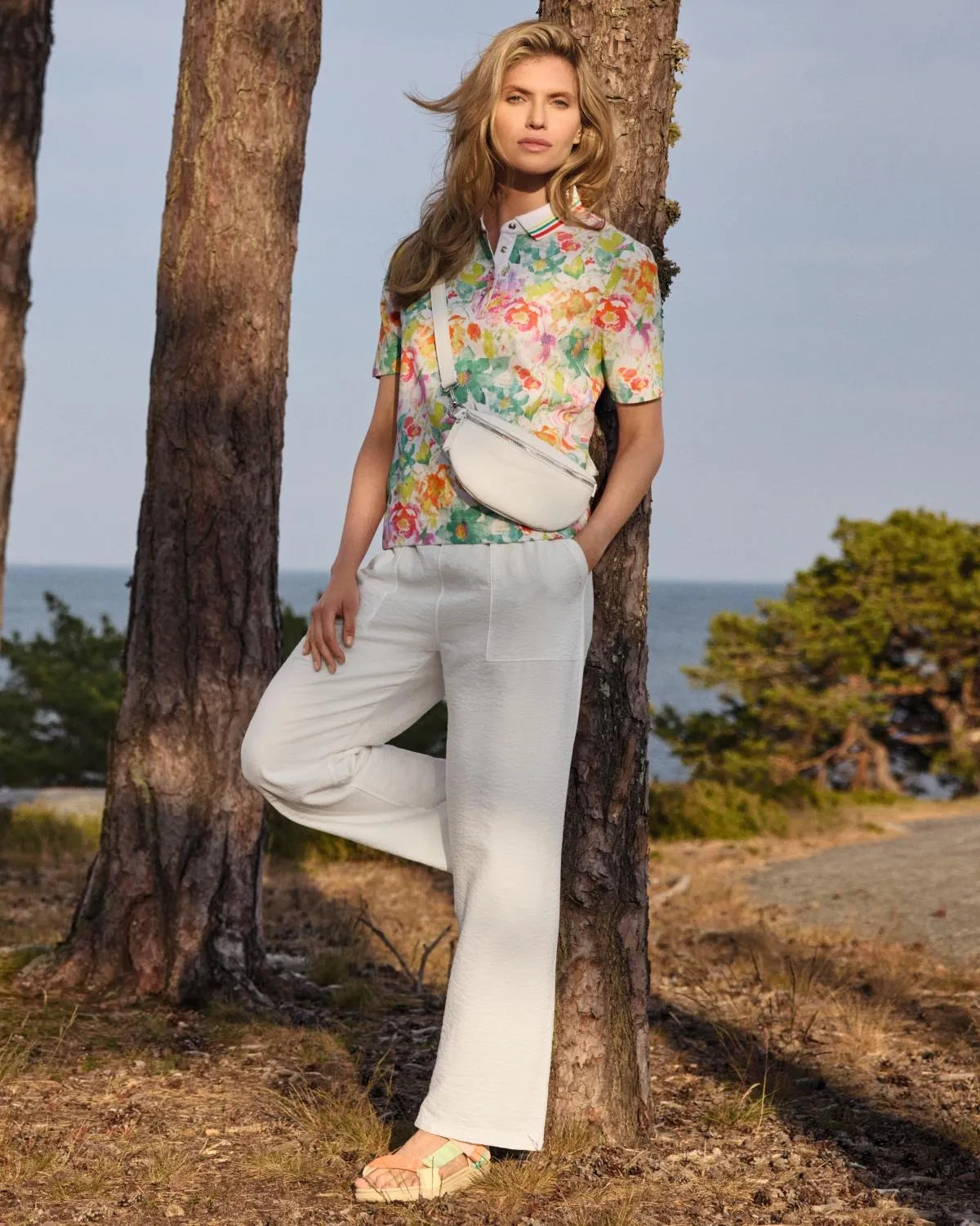 Kurzärmelige Bluse mit Blumenmuster zu einer weißen Hose und einer cremefarbenen Crossbody-Tasche.