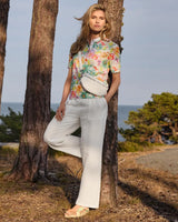 Kurzärmelige Bluse mit Blumenmuster zu einer weißen Hose und einer cremefarbenen Crossbody-Tasche.