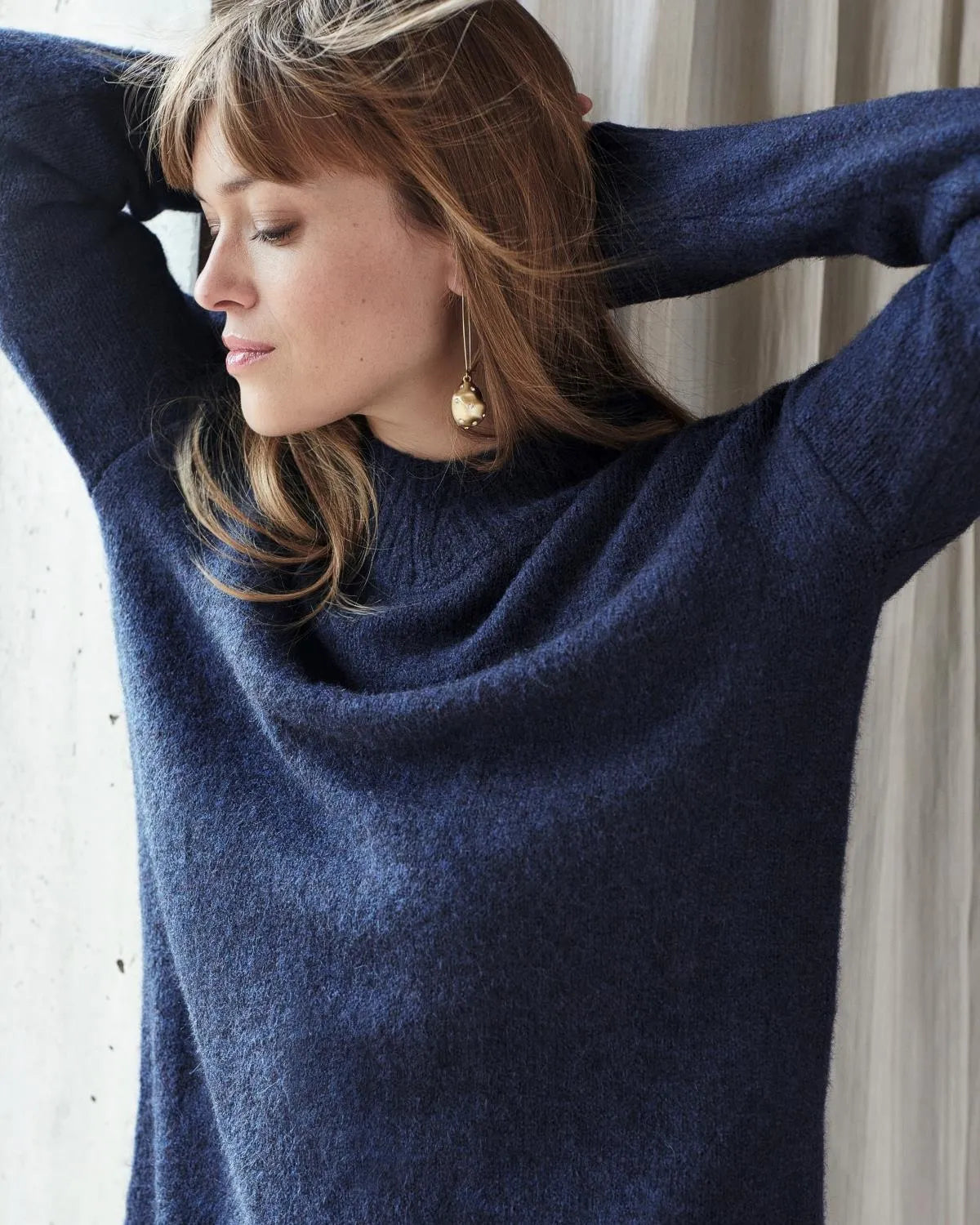 Marineblauer Kaschmirpullover mit Rollkragen und goldenen Ohrringen.