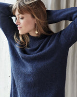 Marineblauer Kaschmirpullover mit Rollkragen und goldenen Ohrringen.